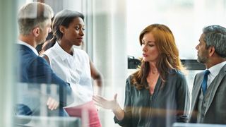 A businesswoman is leading a meeting with three other colleagues. She is talking and they are listening.