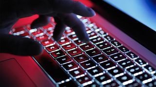 Silhouetted hand typing on an illuminated laptop keyboard.