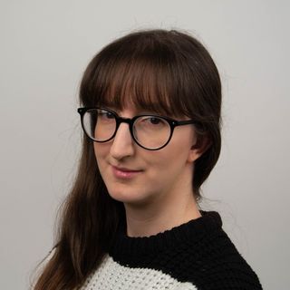 A head and shoulders photo of Jane McCallion, with long brown hair, glasses and a black and white striped jumper